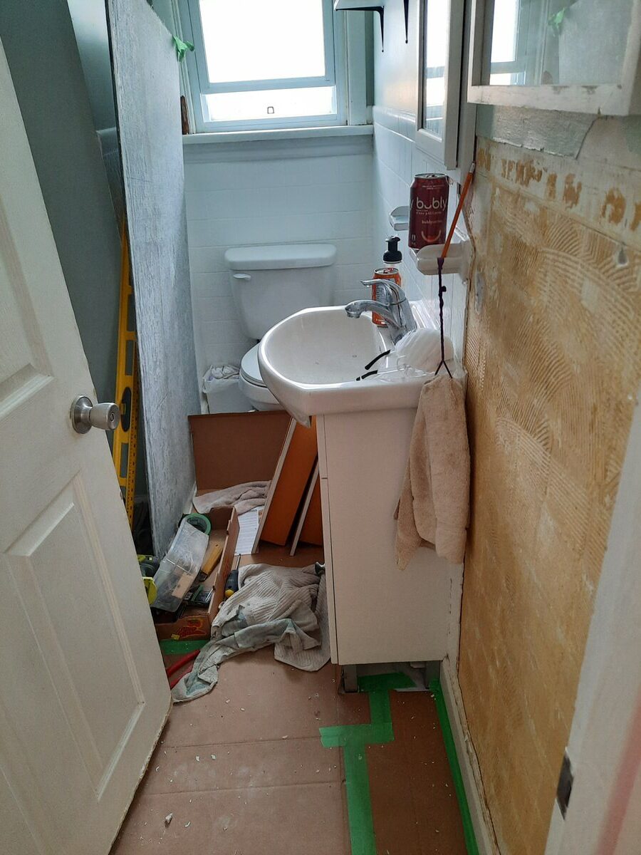 the bathroom before full reno. Walls are torn, bathtub surround is gone, floors covered in cardboard