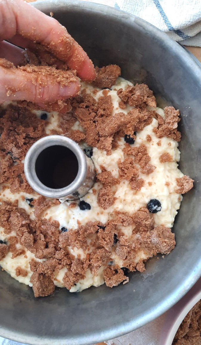 a hand sprinkles crumble on top of the coffee cake batter in the tube pan