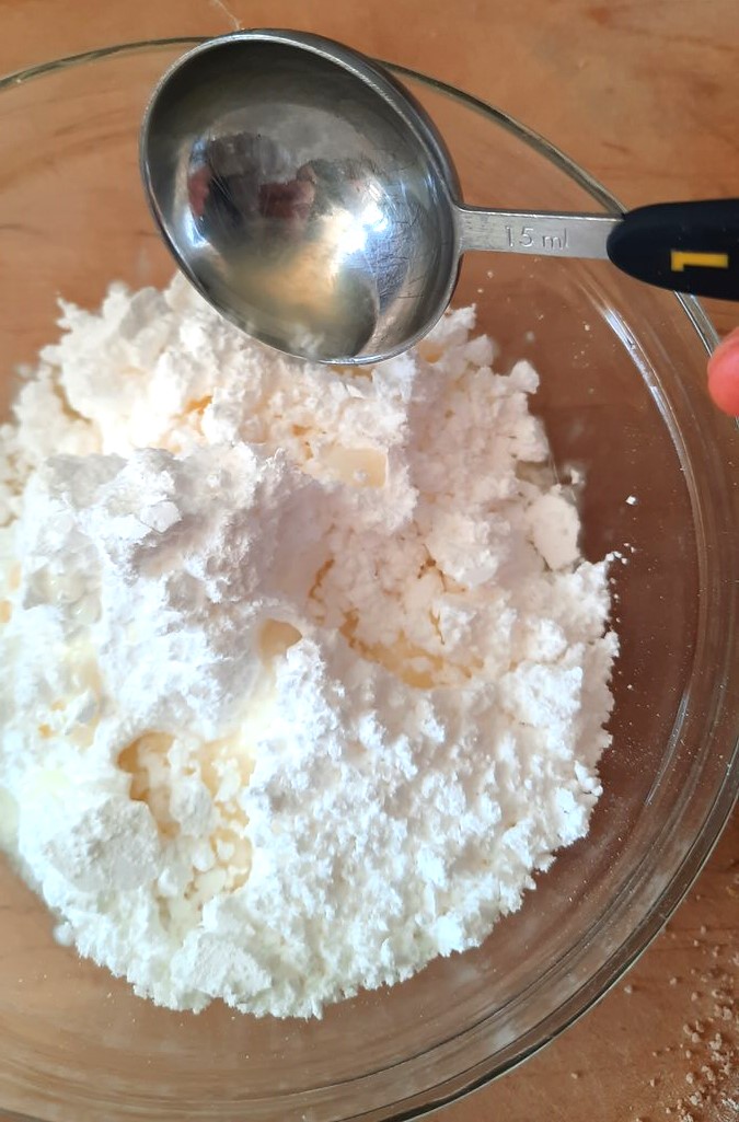 a spoon pours lemon juice into a bowl of icing sugar
