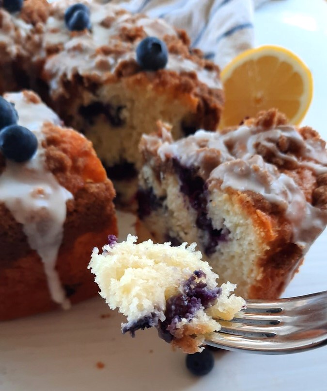 a fork holds up a piece of coffee cake showing its fluffy texture and loads of blueberries