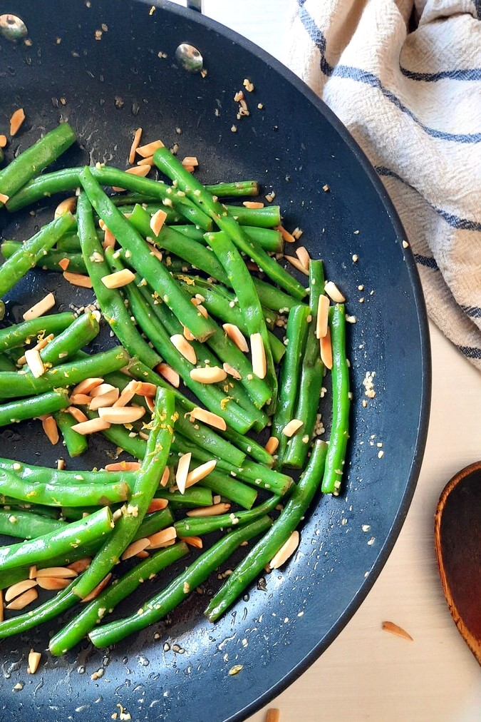 a partial view of a black skillet filled with bright green beans sprinkled with toasted almonds and lemon zest