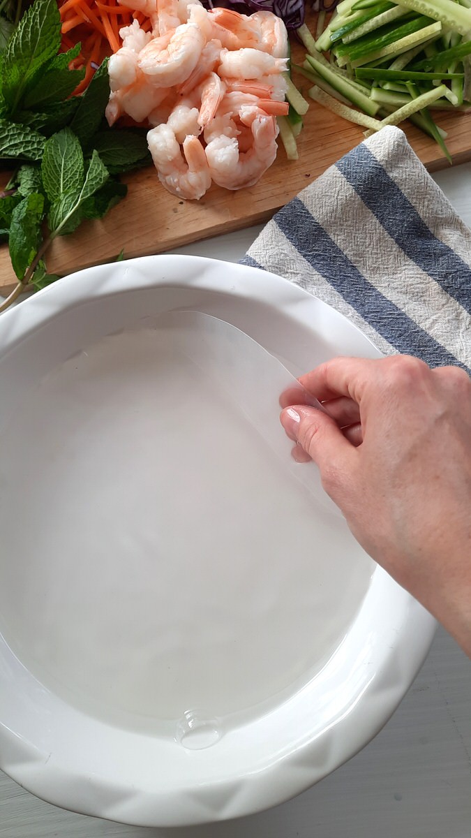a hand places a spring roll wrapper into a shallow dish of warm water