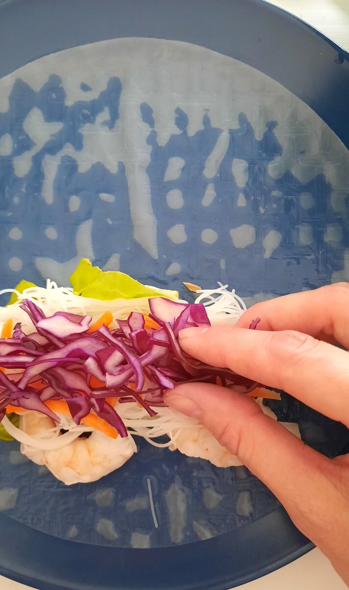 a hand puts shredded red cabbage onto an open spring roll