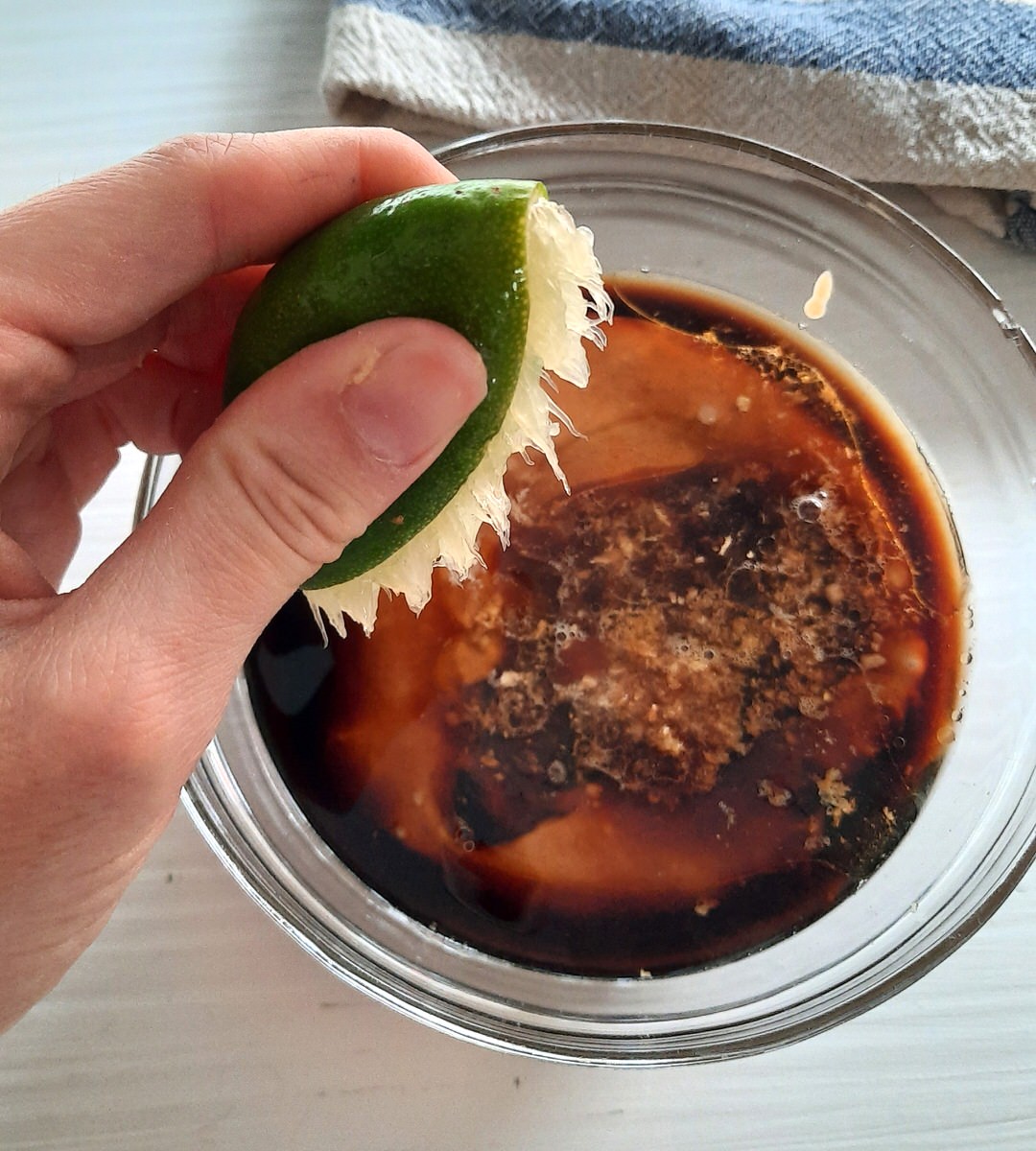 a hand squeezes the juice from a lime into a bowl of peanut dipping sauce