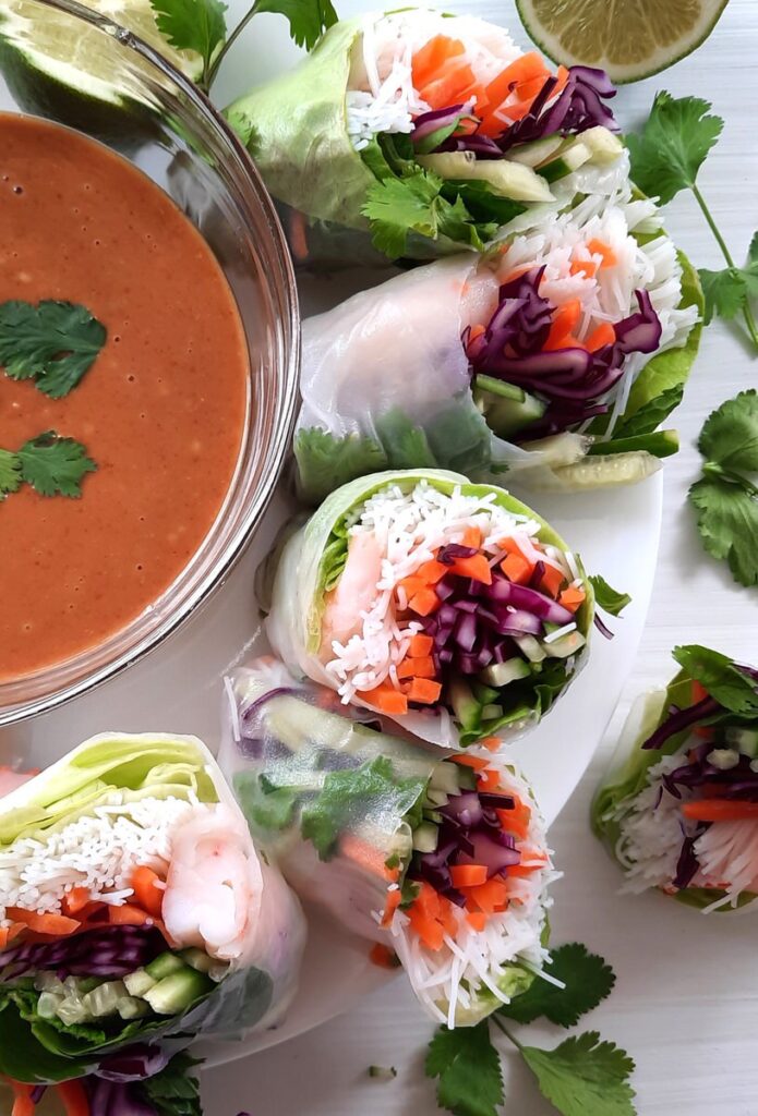 a platter of sliced spring rolls sits beside a bowl of thai peanut dipping sauce