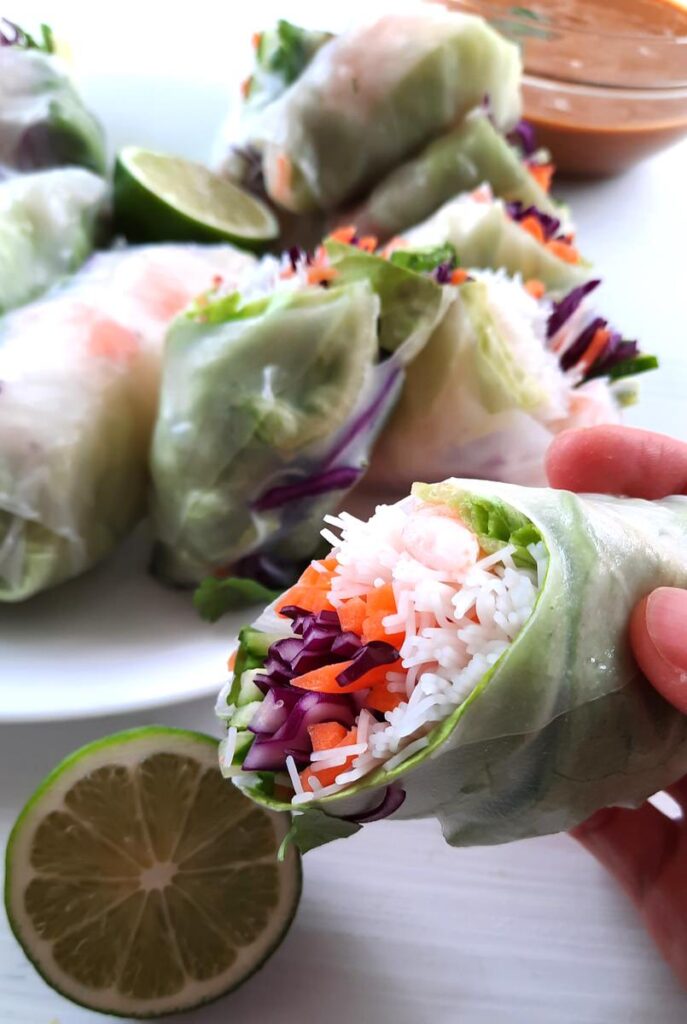 a hand holds a half of a fresh spring roll full of vermicelli noodles, vegetables, and shrimp