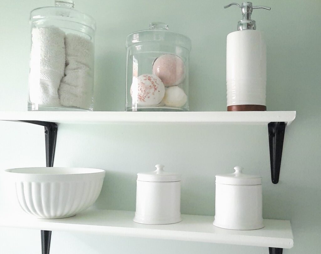white wood shelves hang on a soft green wall holding an array of pretty jars