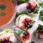 a close up of halved fresh spring rolls beside a bowl of peanut dipping sauce