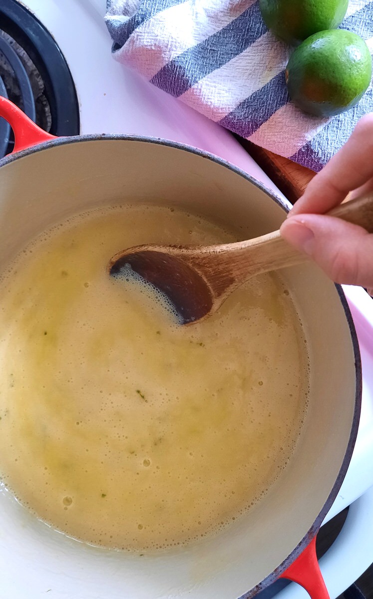 a hand stirs lime curd on the stove with a wooden spoon
