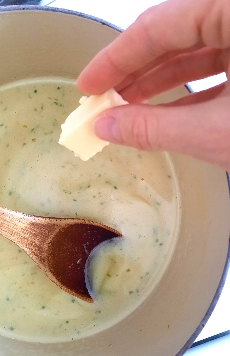 a hand drops a tablespoon of butter into a pot of warm lime curd